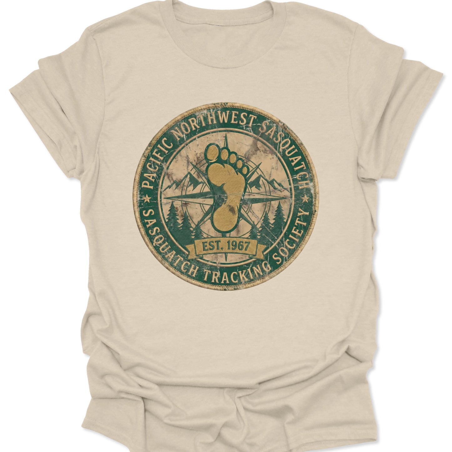 Natural unisex adult t-shirt featuring a retro Pacific Northwest Sasquatch badge with a large yellow footprint and compass rose.