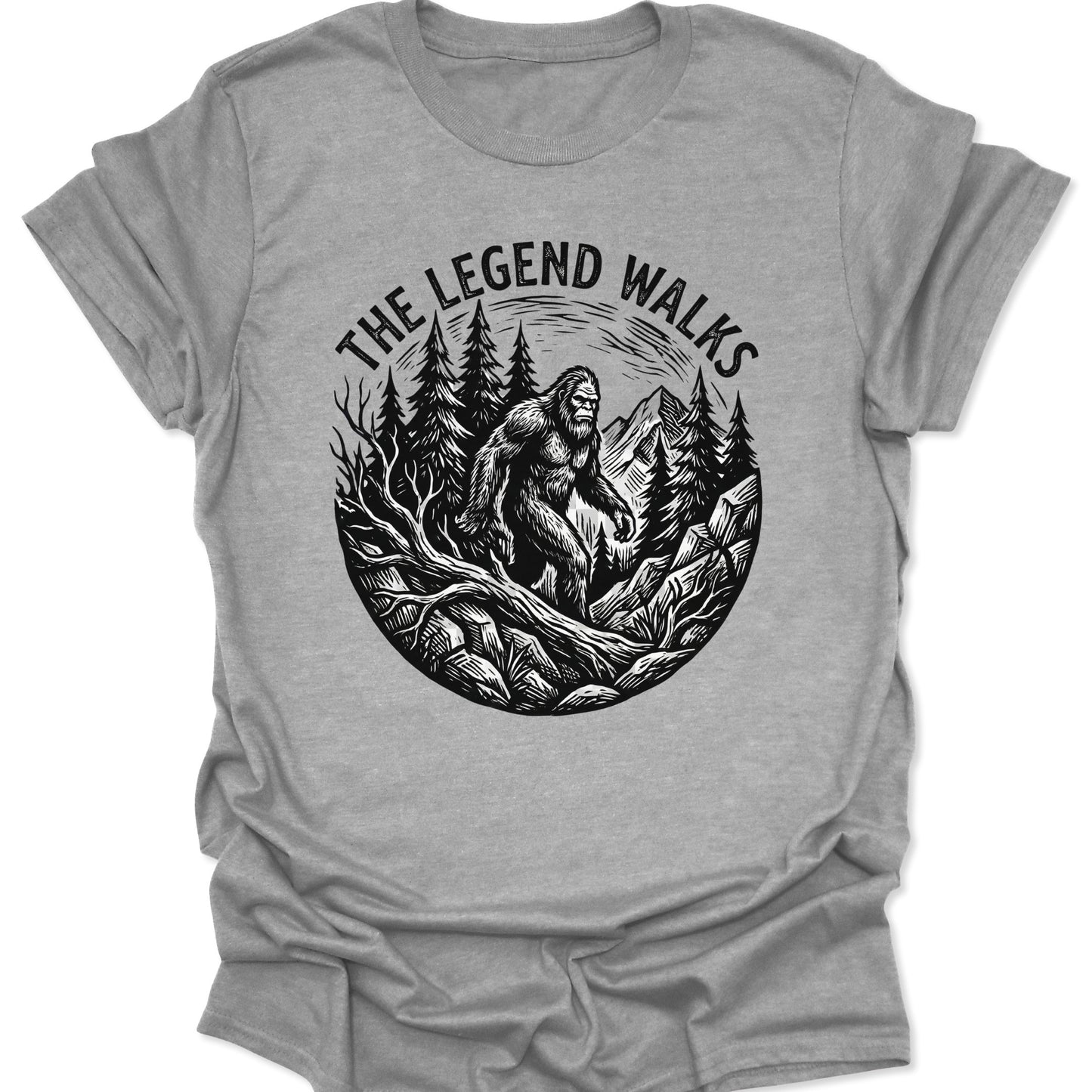 Sport Grey unisex adult t-shirt featuring a black woodcut Sasquatch walking through a pine forest with mountains.
