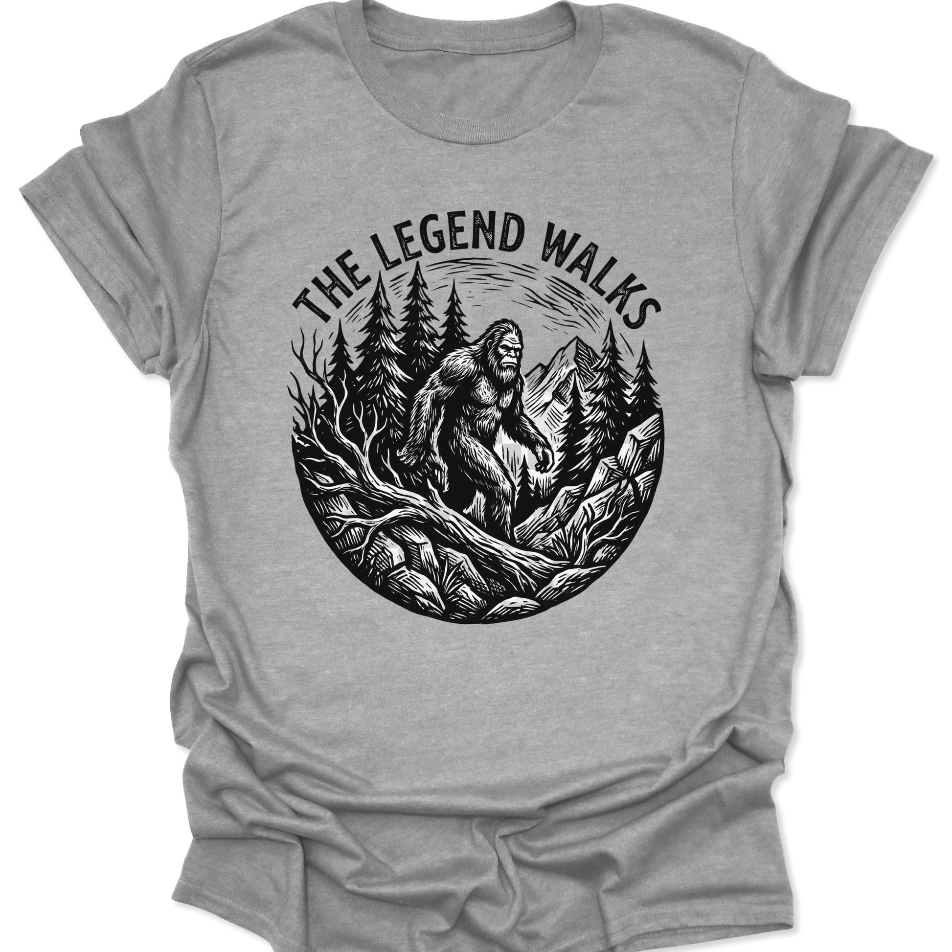 Sport Grey unisex adult t-shirt featuring a black woodcut Sasquatch walking through a pine forest with mountains.