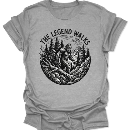 Sport Grey unisex adult t-shirt featuring a black woodcut Sasquatch walking through a pine forest with mountains.