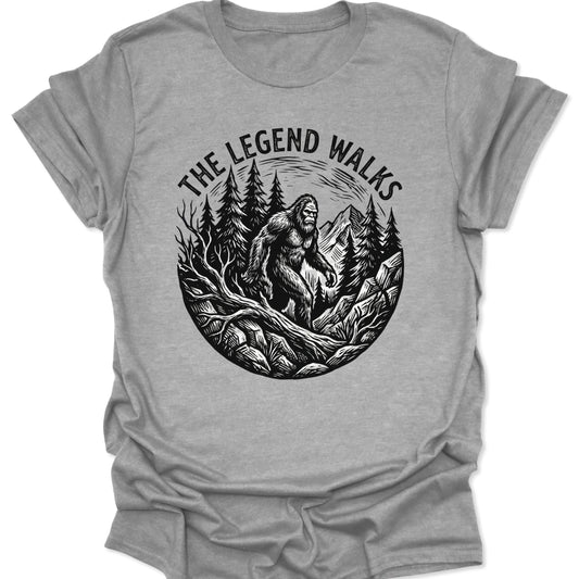 Sport Grey unisex adult t-shirt featuring a black woodcut Sasquatch walking through a pine forest with mountains.