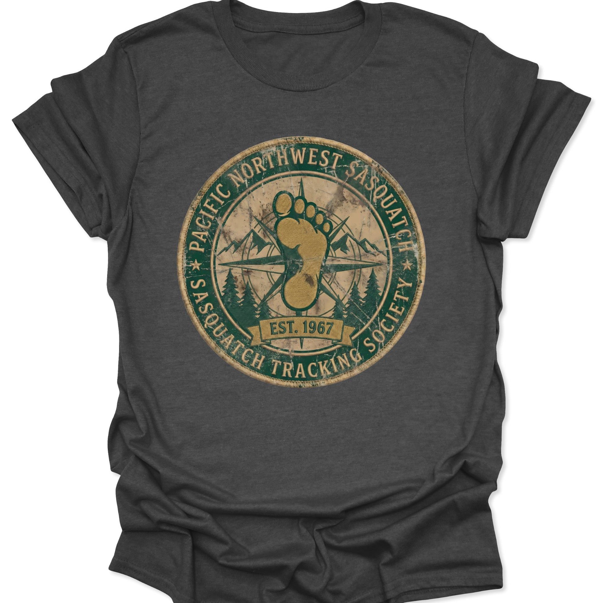 Dark heather unisex adult t-shirt featuring a vintage distressed Bigfoot seal with PNW forest silhouettes and mountain peaks.