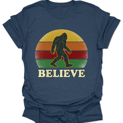 Heather navy unisex adult t-shirt featuring a distressed Bigfoot silhouette walking across a retro striped sunset.