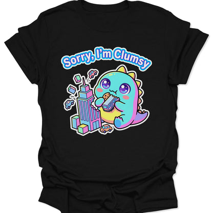 Black unisex adult t-shirt featuring a pastel chibi kaiju eating a bus with "Sorry, I'm Clumsy" text in bubbly letters.