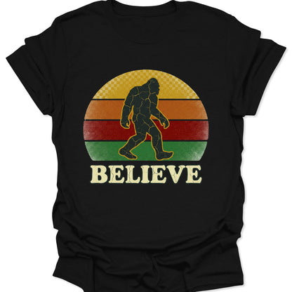 Black unisex adult t-shirt with a vintage "Believe" Sasquatch graphic in a weathered yellow, orange, and green circle.