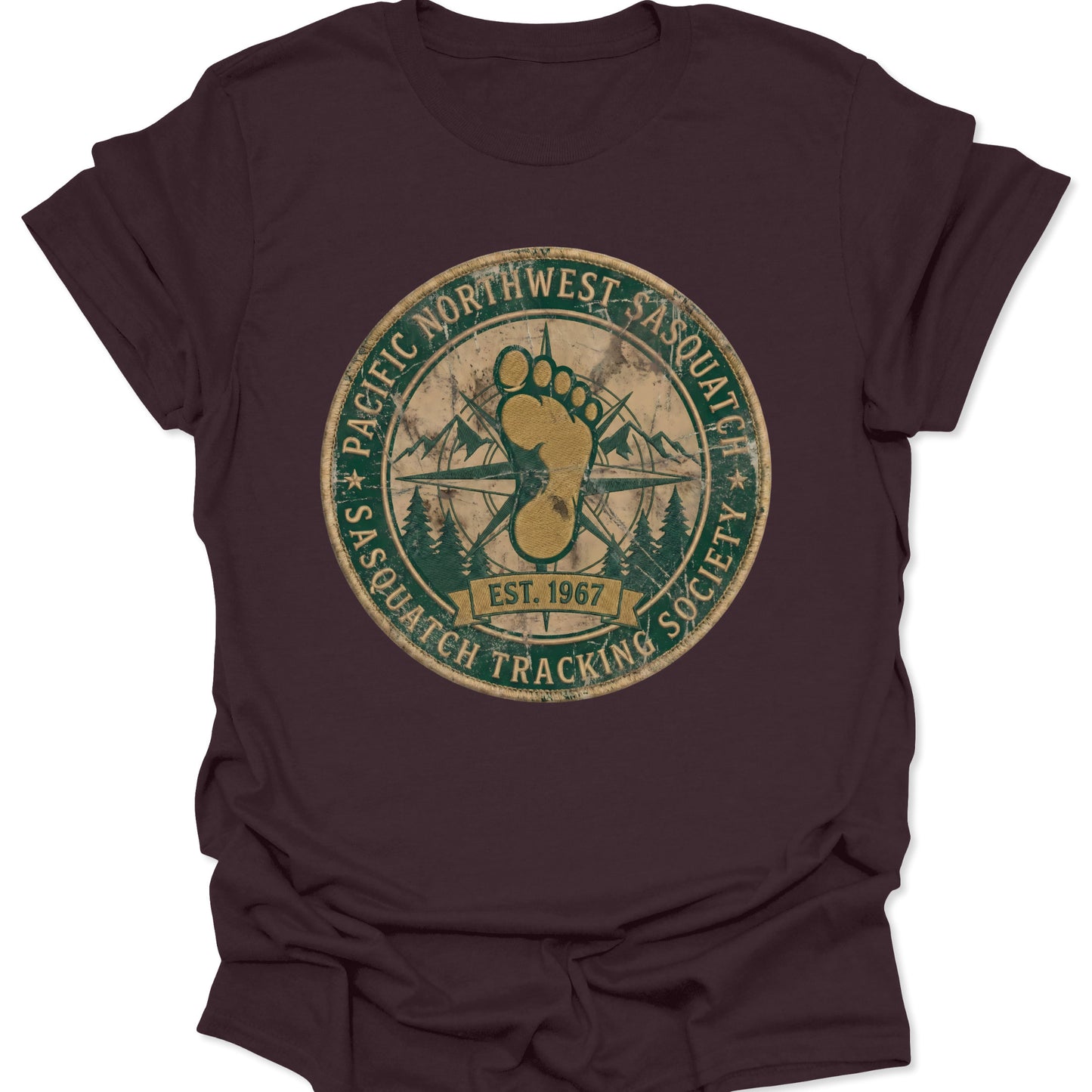 Dark chocolate unisex adult t-shirt featuring a weathered green Sasquatch Tracking Society seal with a gold footprint and compass.