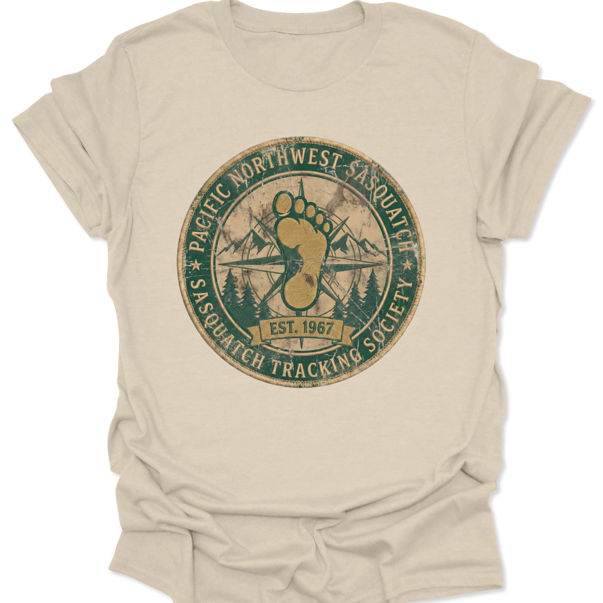 Natural unisex adult t-shirt featuring a retro Pacific Northwest Sasquatch badge with a large yellow footprint and compass rose.