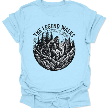 Light Blue unisex adult t-shirt featuring a black ink-style Bigfoot legend walking through a Pacific Northwest wilderness.